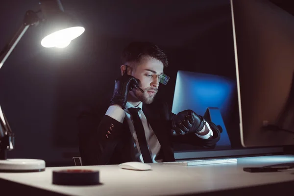 Retrato de agente espião em luvas com fone de ouvido tempo de verificação na mesa com tela do computador no escuro — Fotografia de Stock