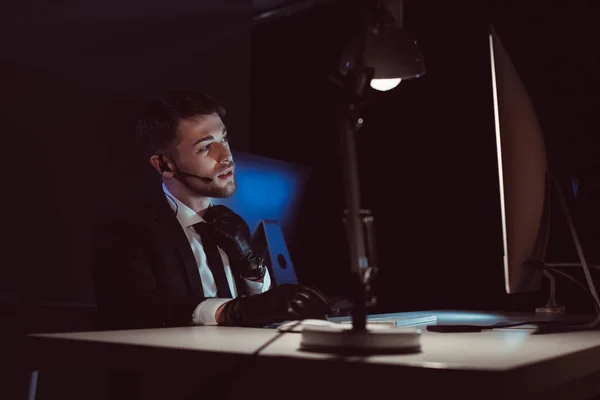 Spy agent in gloves with headset sitting at table in dark — Stock Photo