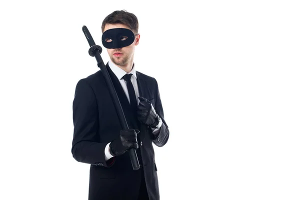 Agente espía en máscara y guantes con katana mirando hacia otro lado aislado en blanco - foto de stock