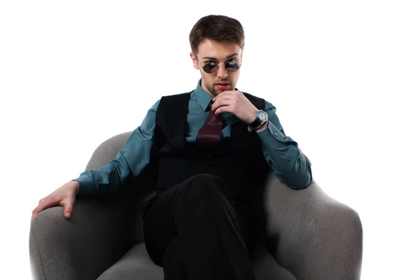 Portrait of pensive stylish spy in sunglasses sitting in armchair isolated on white — Stock Photo