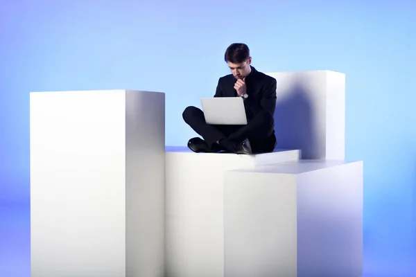 Businessman using laptop while sitting on white block isolated on white — Stock Photo