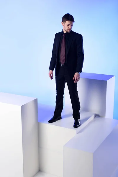 Businessman in black suit standing on white block isolated on blue — Stock Photo