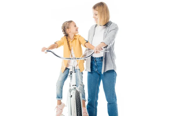 Smiling mother and cute daughter on bicycle looking at each other isolated on white — Stock Photo