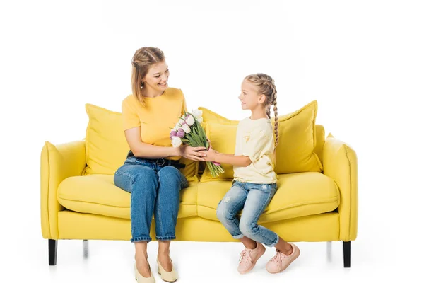 Kleines Kind schenkt Tulpenstrauß an Mutter auf gelbem Sofa isoliert auf weißem, Muttertagsferienkonzept — Stockfoto