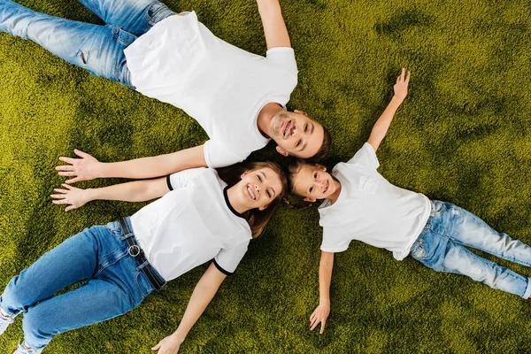 Overhead view of happy family in similar clothing lying on green lawn — Stock Photo