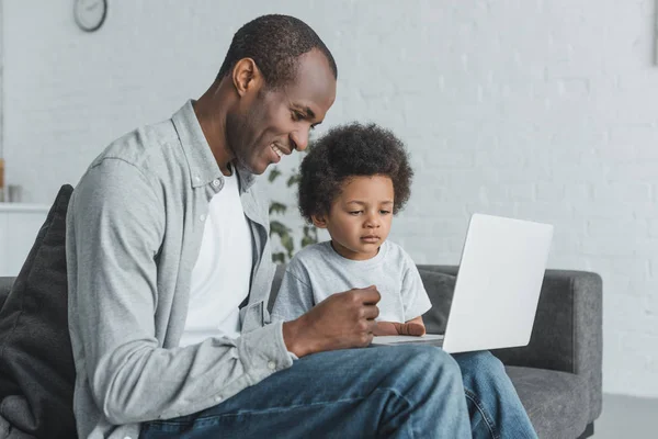 Vue latérale du père afro-américain regardant quelque chose à l'ordinateur portable avec son fils à la maison — Photo de stock