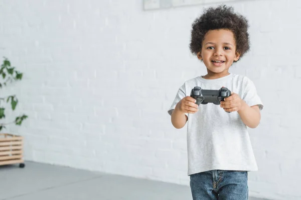 Sorrindo adorável menino afro-americano de pé com joystick em casa — Fotografia de Stock