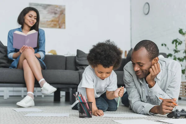 African american father drawing with son and mother reading book at home — Stock Photo