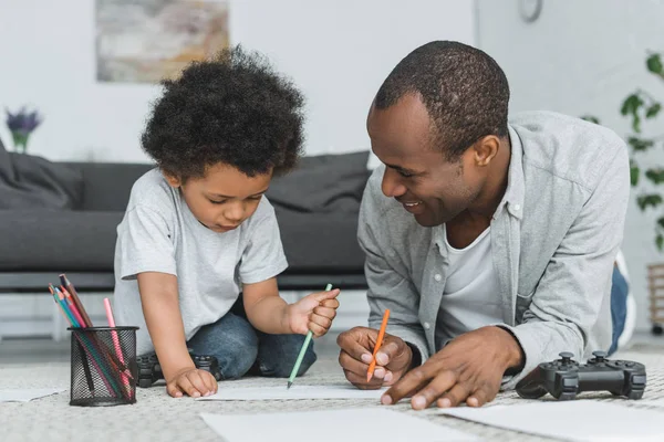Africano americano padre dibujo con hijo en piso en casa - foto de stock
