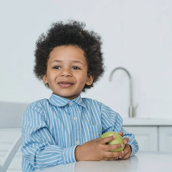 Entzückender afrikanischer amerikanischer Junge mit Apfel am Tisch in der Küche — Stockfoto