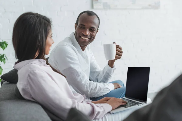 Afroamericana novia usando laptop y novio bebiendo café en casa - foto de stock