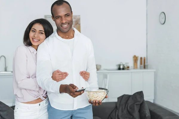 African american girlfriend hugging boyfriend with popcorn at home — Stock Photo