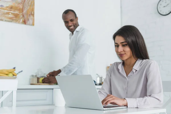 African american girlfriend using laptop and boyfriend cooking at kitchen — Stock Photo