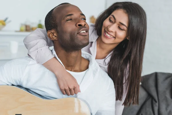 Novio afroamericano tocando la guitarra y cantando para su novia en casa - foto de stock