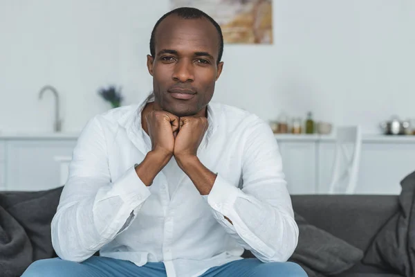 Schöner afrikanisch-amerikanischer Mann, der sein Kinn auf die Hände legt und zu Hause in die Kamera schaut — Stockfoto