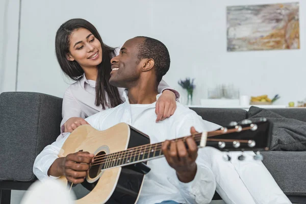 Lächelnder afrikanisch-amerikanischer Freund spielt zu Hause Gitarre für Freundin — Stockfoto