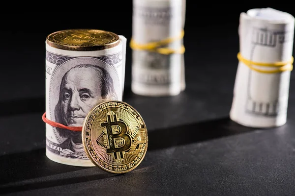 Close-up view of rolled dollar banknotes and bitcoins on black — Stock Photo