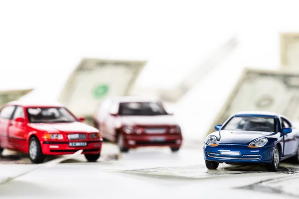 Крупный план небольших моделей автомобилей и долларовых купюр на белом — стоковое фото