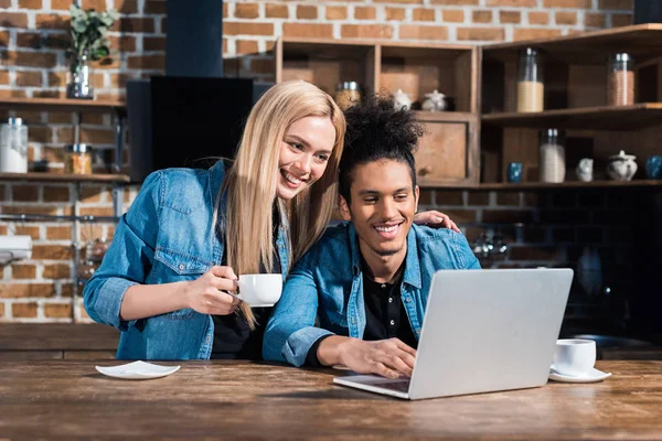 Sorrindo casal multirracial usando laptop juntos na cozinha em casa — Fotografia de Stock