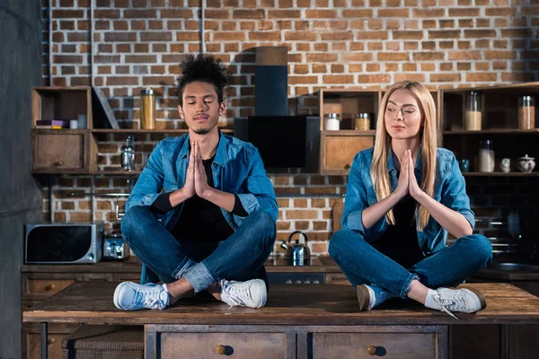 Casal multirracial sentado em posição de lótus na cozinha em casa — Fotografia de Stock