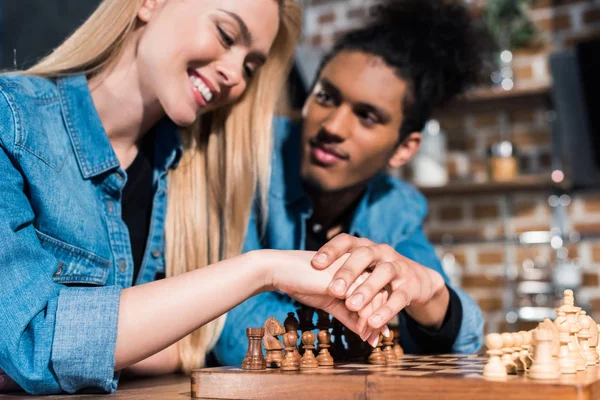 Focus selettivo della giovane coppia multietnica che gioca a scacchi insieme in cucina — Foto stock