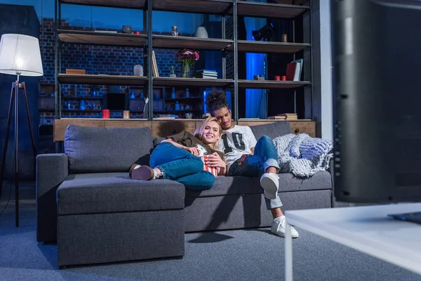 Jovem casal multirracial com pipocas assistindo filme no sofá juntos em casa — Fotografia de Stock