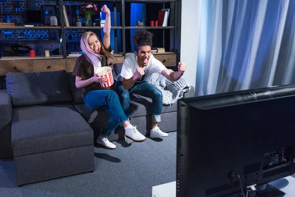 Emotionales multirassisches Paar mit Popcorn, das zu Hause zusammen auf dem Sofa ein Fußballspiel anschaut — Stockfoto