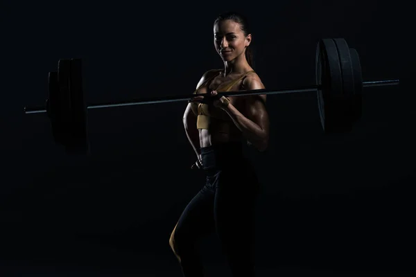 Beautiful female bodybuilder posing with barbell, isolated on black — Stock Photo
