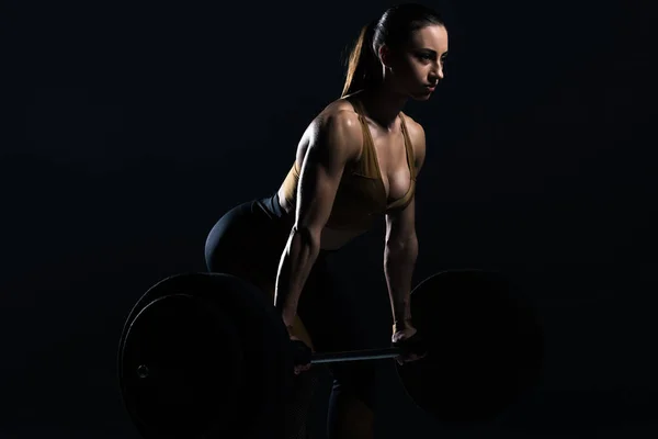 Beautiful female bodybuilder lifting barbell, isolated on black — Stock Photo