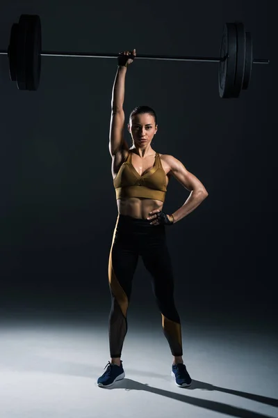Giovane bodybuilder forte che tiene il bilanciere, su nero — Foto stock