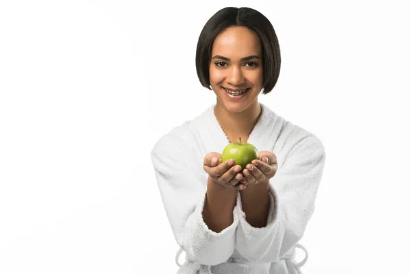 Усміхнена афроамериканська дівчина з зубними брекетами, що тримає яблуко, ізольована на білому — стокове фото