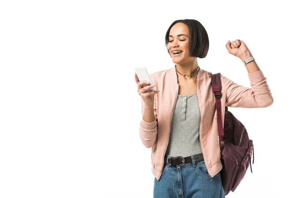 Aufgeregten afrikanisch-amerikanischen Studentin mit Rucksack mit Smartphone, isoliert auf weiß — Stockfoto