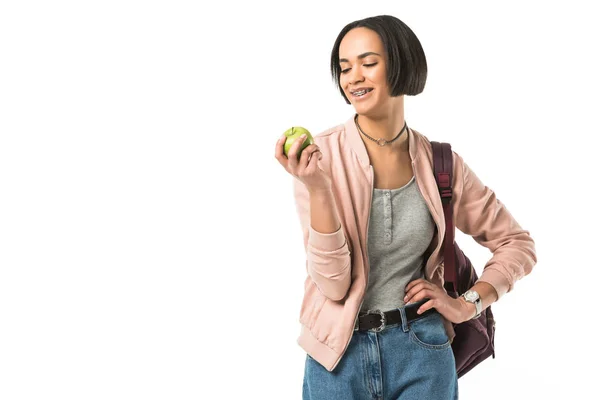 Estudiante afroamericana sonriente con mochila sosteniendo manzana, aislada en blanco - foto de stock