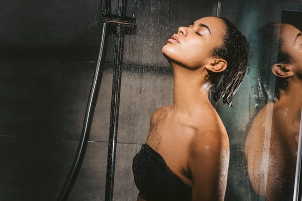 Atractivo afroamericano chica con los ojos cerrados tomando ducha - foto de stock