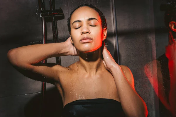 Attraente donna afroamericana con gli occhi chiusi lavare i capelli in doccia — Foto stock