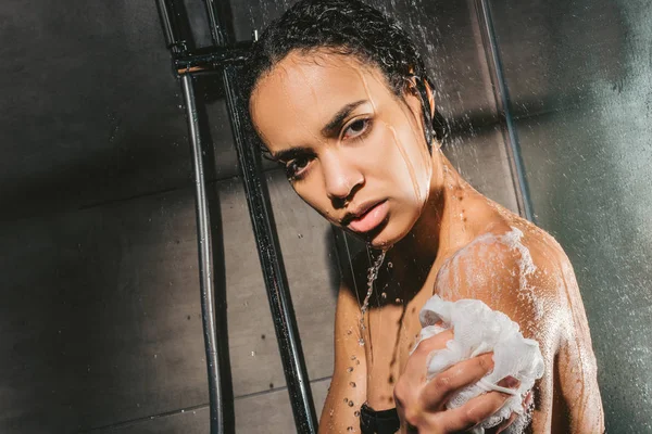 Bella donna afro-americana che fa la doccia con schiuma e spugna — Foto stock