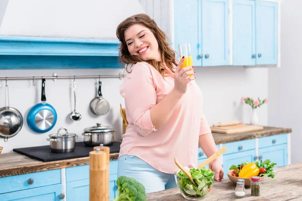 Porträt einer übergewichtigen lächelnden Frau mit einem Glas Saft in der heimischen Küche — Stockfoto