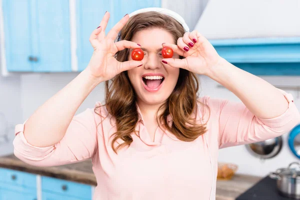 Затемнений вигляд надмірної ваги жінки в навушниках з вишневими помідорами в руках на кухні — стокове фото