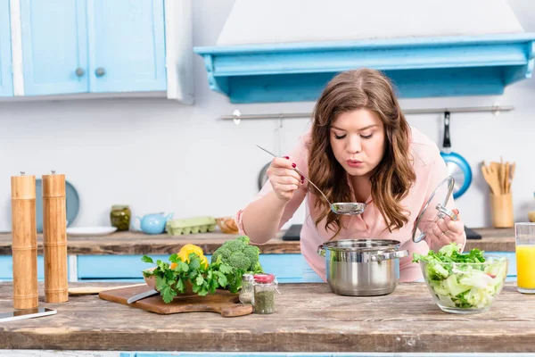 Ritratto di giovane donna sovrappeso che cucina zuppa in cucina a casa — Foto stock