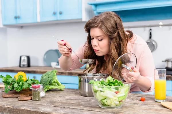 Retrato de jovem mulher com sobrepeso cozinhar sopa na cozinha em casa — Fotografia de Stock