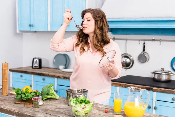 Ritratto di giovane donna sovrappeso che cucina zuppa in cucina a casa — Foto stock