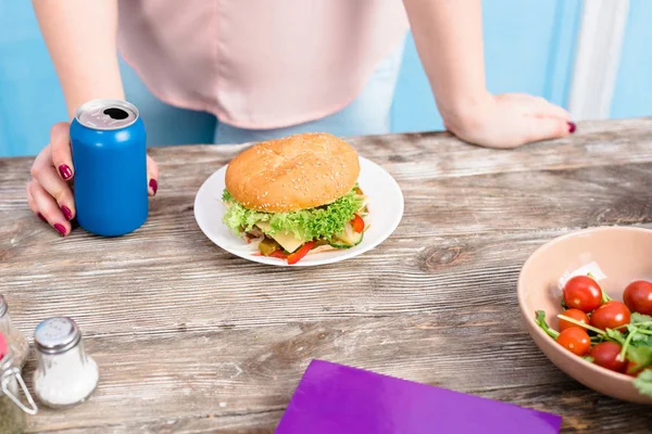 Colpo ritagliato di donna in sovrappeso con bibita gassata in piedi al tavolo con hamburger — Foto stock