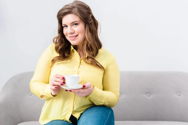 Портрет улыбающейся женщины с чашкой кофе, сидящей дома на диване — стоковое фото