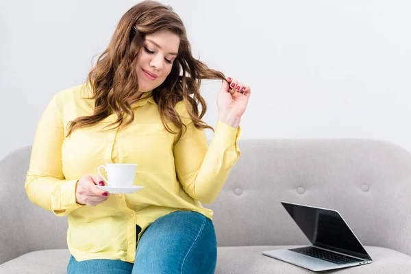Портрет жінки з чашкою кави, що сидить на дивані з ноутбуком вдома — стокове фото