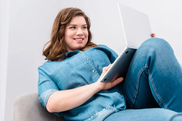 Молодая улыбающаяся женщина с ноутбуком на диване дома — стоковое фото