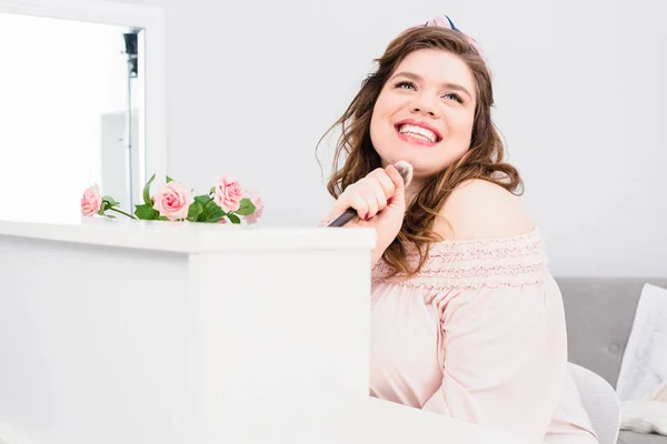 Emotional young woman singing with makeup brush in hand as microphone at home — Stock Photo