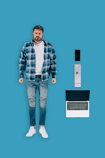 Top view of stressed remote worker with smartphone, remote controller and laptop isolated on blue background — Stock Photo