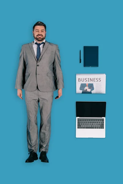 Vista superior del hombre de negocios con ordenador portátil, periódico, libro de texto y pluma aislado sobre fondo azul - foto de stock