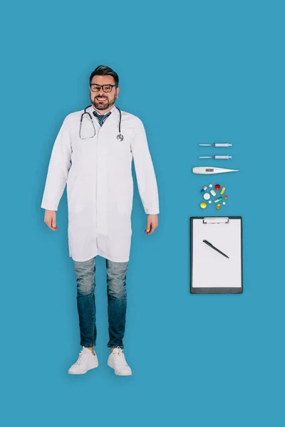 Вид зверху чоловічий лікар зі стетоскопом, таблетками, буферами, шприцами, термометром ізольовані на синьому фоні — стокове фото