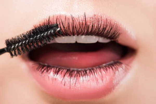 Cropped image of woman applying black mascara on eyelashes in mouth isolated on white — Stock Photo